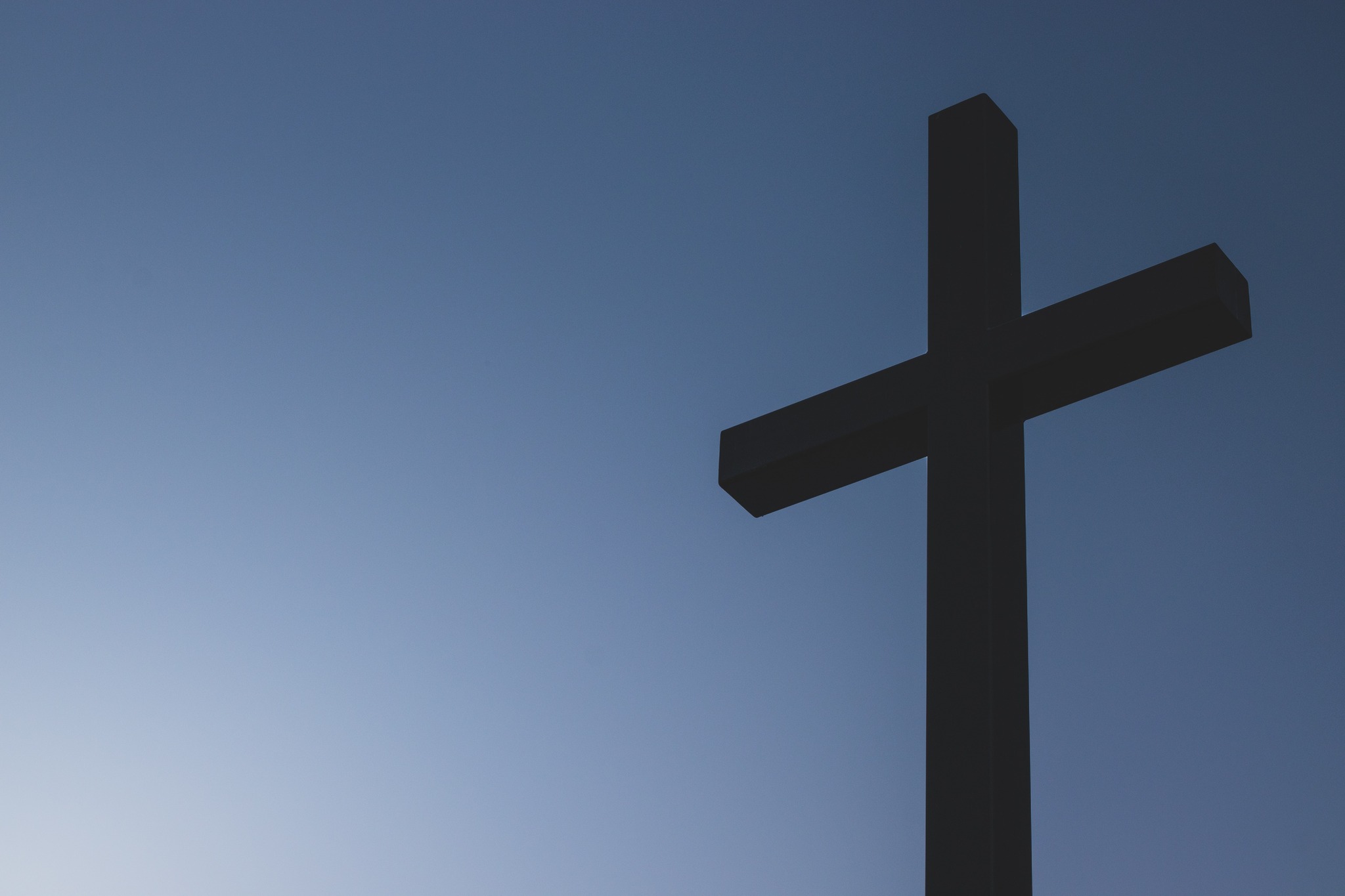 Cross silhouette against a deep blue Alberta sky — symbol of faith and hope